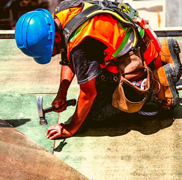 Ouvrier de construction utilisant un marteau pour installer une surface sur un chantier avec équipement de sécurité