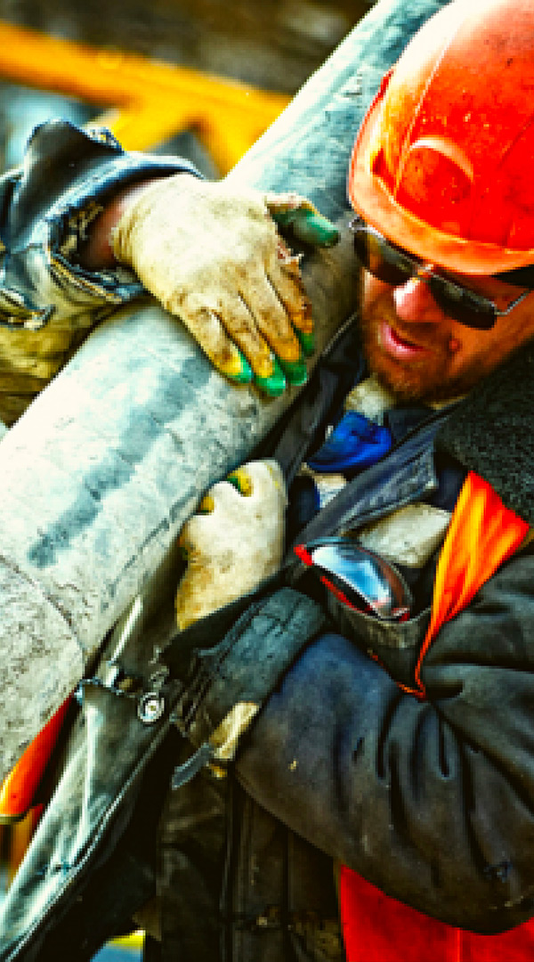 Ouvrier de construction manipulant un tuyau sur un chantier avec équipement de sécurité et casque de protection